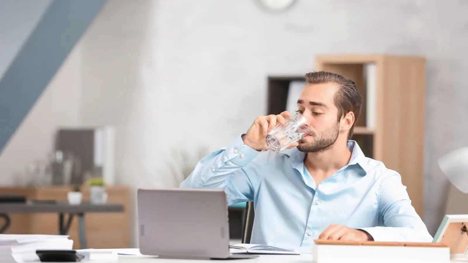 man drinking water while sitting in front of laptop